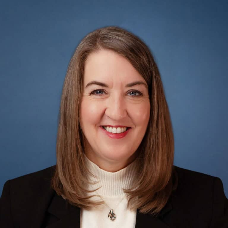 Headshot of Dala Bebee smiling, wearing a black blazer and white turtleneck.