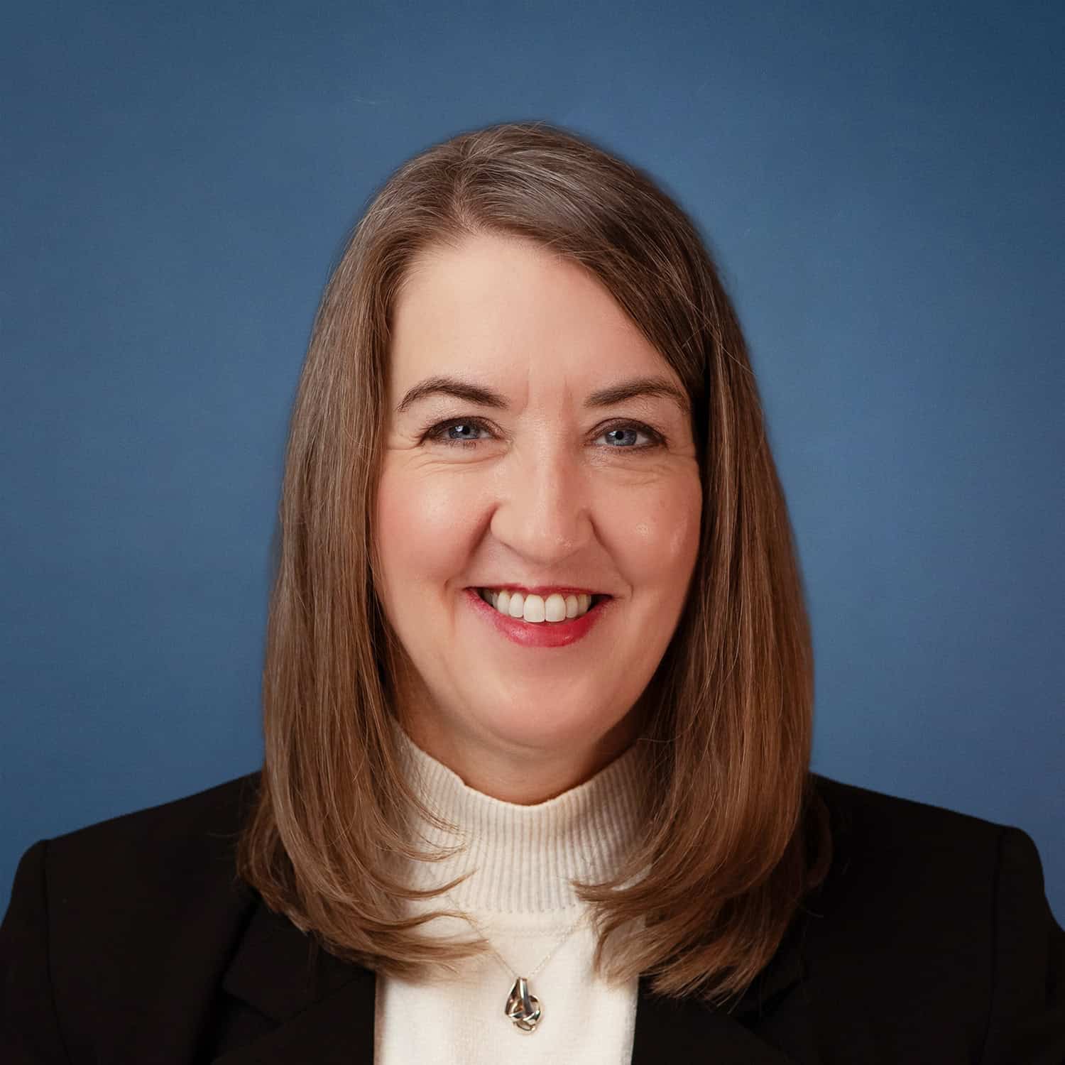 Headshot of Dala Bebee smiling, wearing a black blazer and white turtleneck.