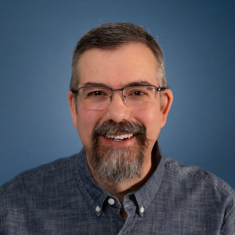 Headshot of Jason Krogmann with glasses and a beard against a blue background.
