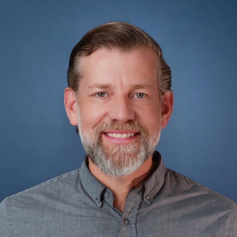 Nathan Miller smiling in a gray shirt with a blue background.