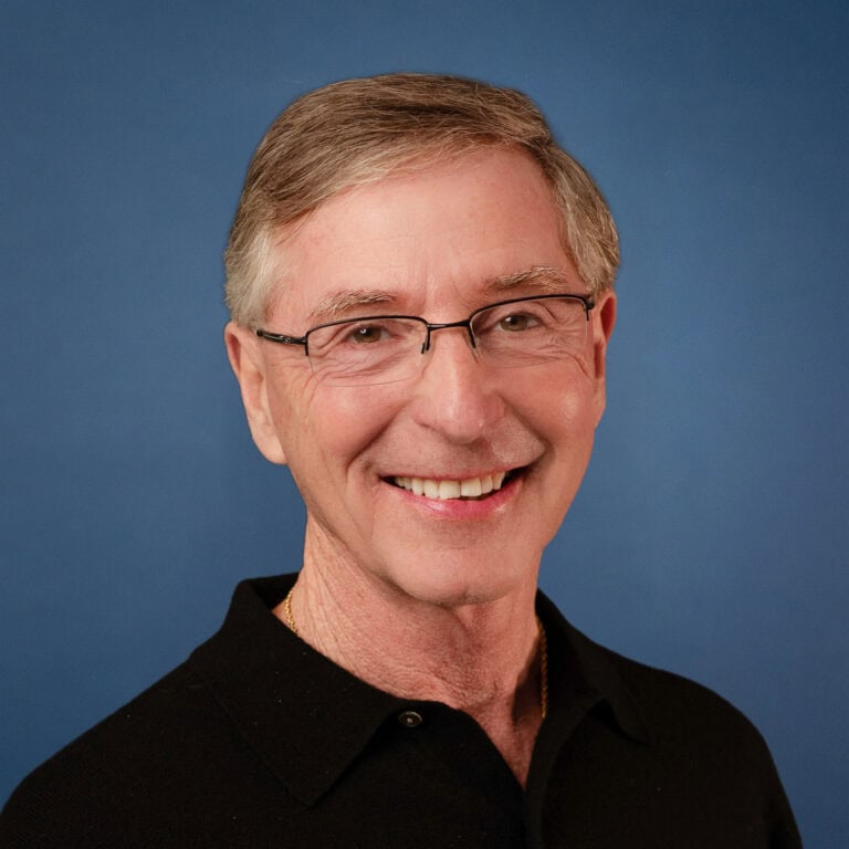 Headshot of Tom Nelson smiling, wearing glasses and a black shirt.
