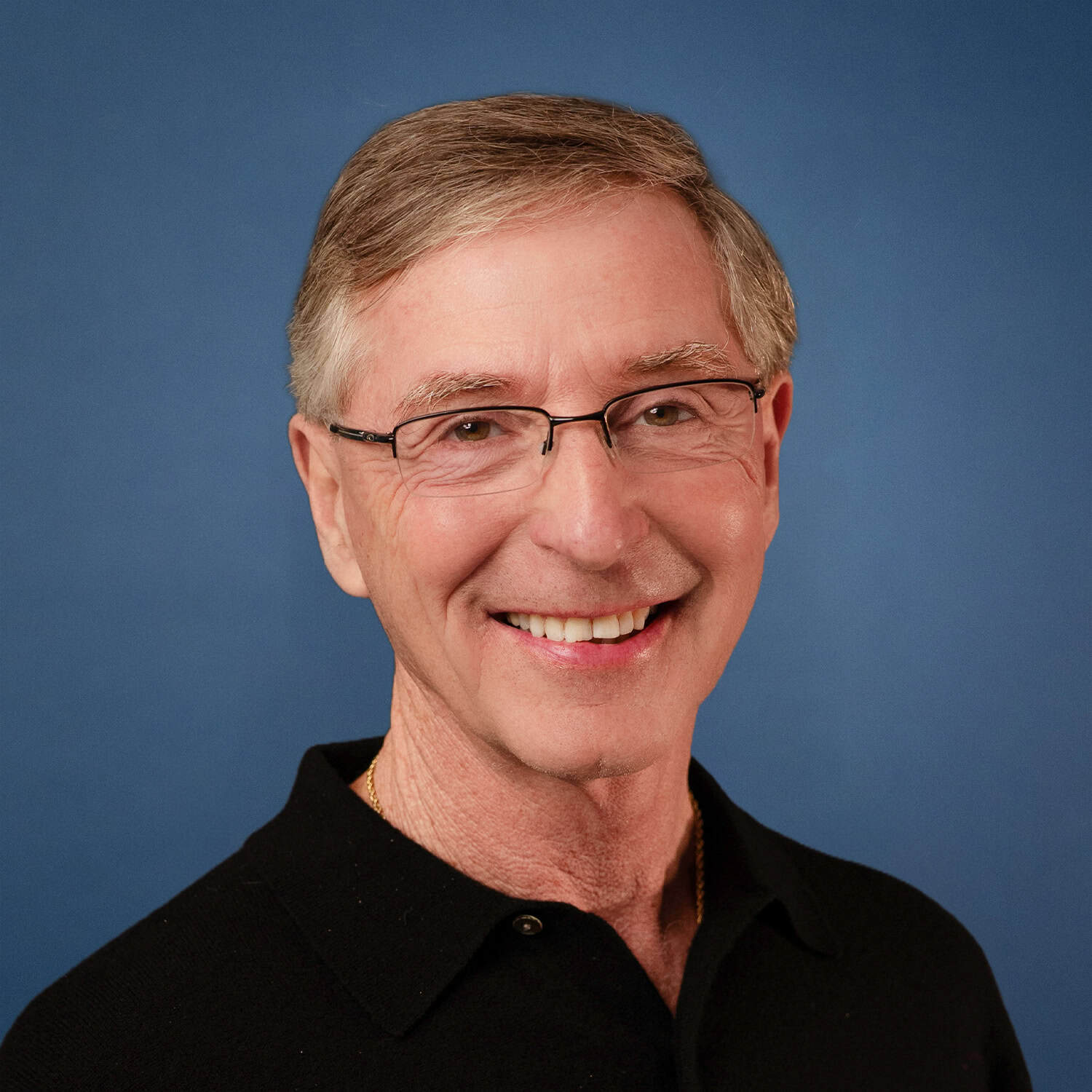 Headshot of Tom Nelson smiling, wearing glasses and a black shirt.