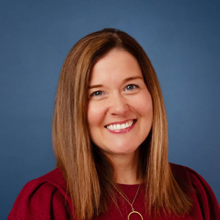 Anna Lynn Rolf smiles in a professional headshot with a blue background.