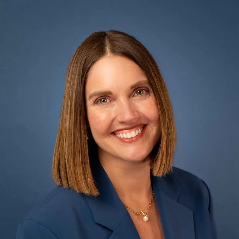 Holly Justice smiles in a professional headshot with a blue blazer and gold necklace.