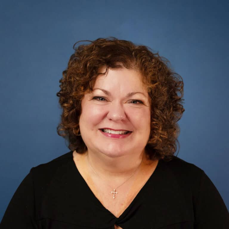 Melissa Bennett smiles in a headshot with curly hair against a blue background.