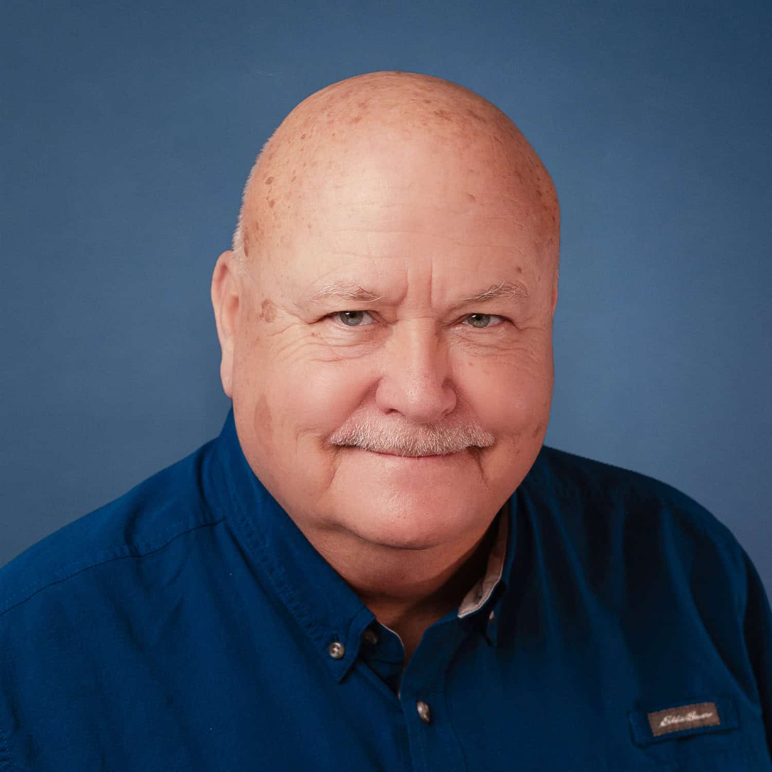 Portrait of Warren Traynor wearing a blue shirt against a blue background.
