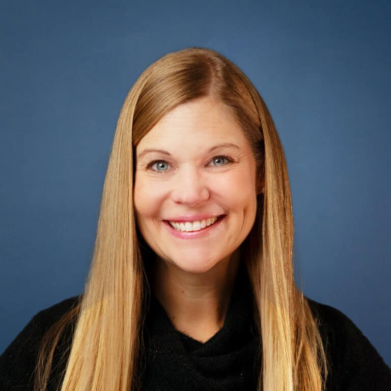Portrait of Carolyn Poage smiling against a blue background.