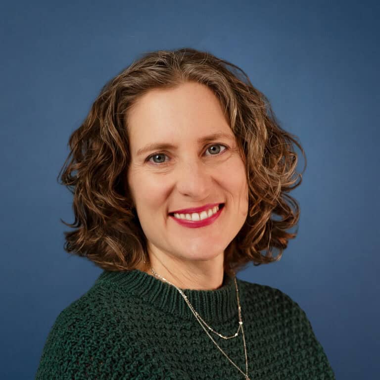 Portrait of Nikki Dieker, smiling with curly hair and wearing a green sweater.
