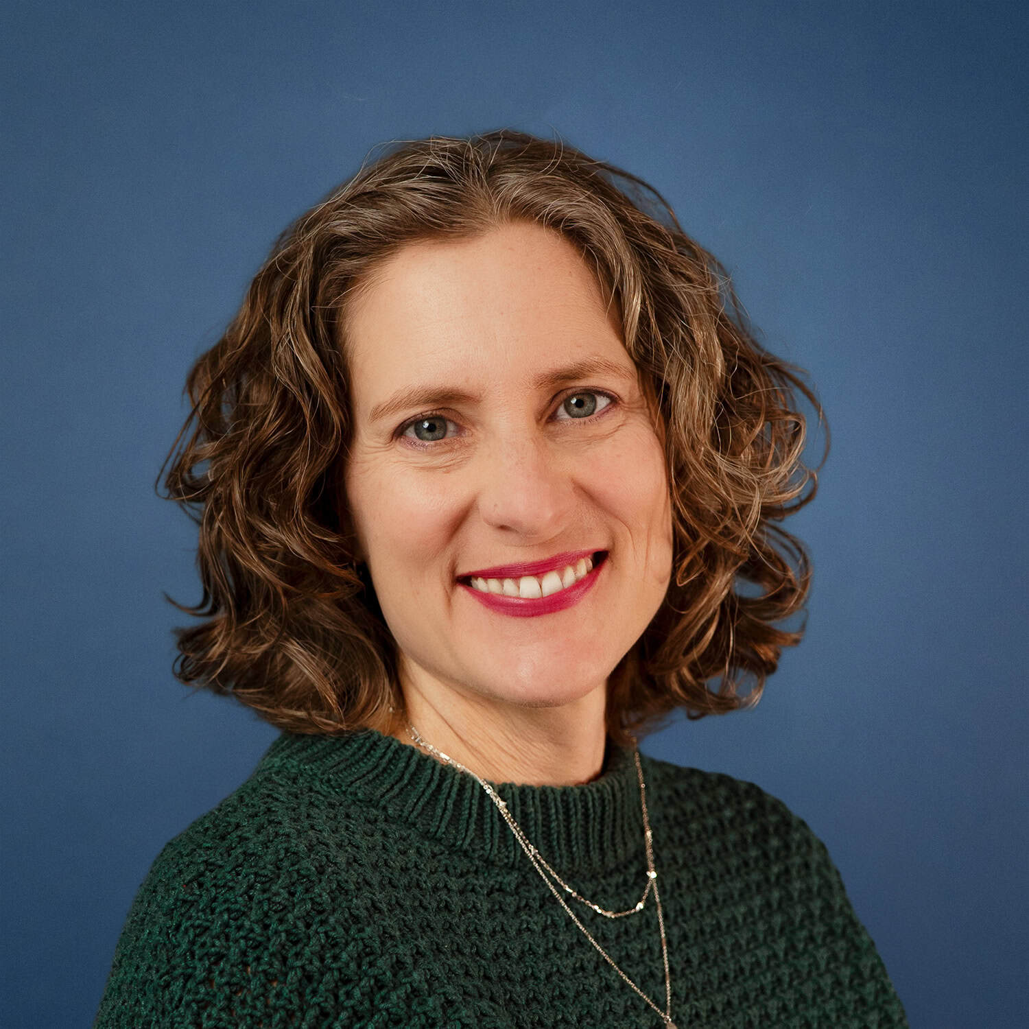 Portrait of Nikki Dieker, smiling with curly hair and wearing a green sweater.