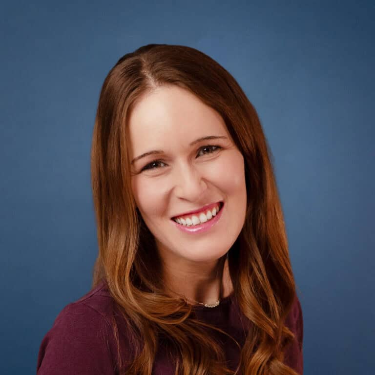 Chelsey Keim smiles warmly, a headshot on a blue background.