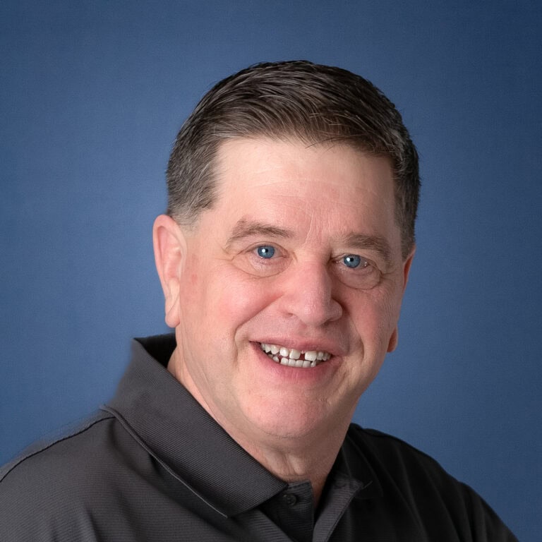 Headshot of Dean Parker smiling against a blue background.