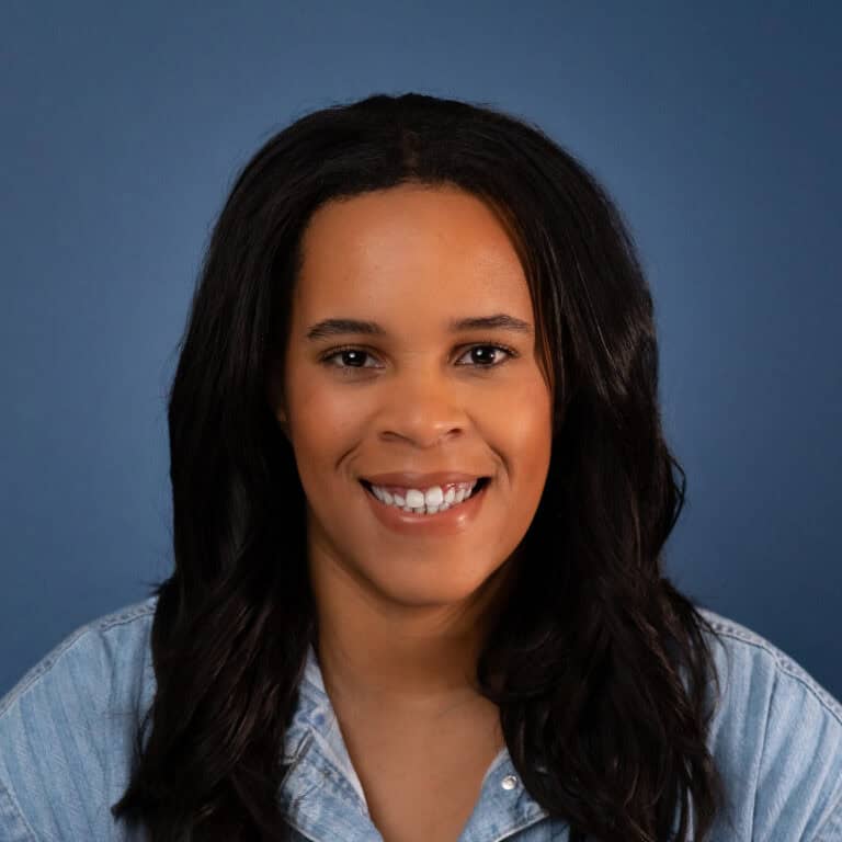 Akilah Boone smiles in a headshot, wearing a denim shirt against a blue background.