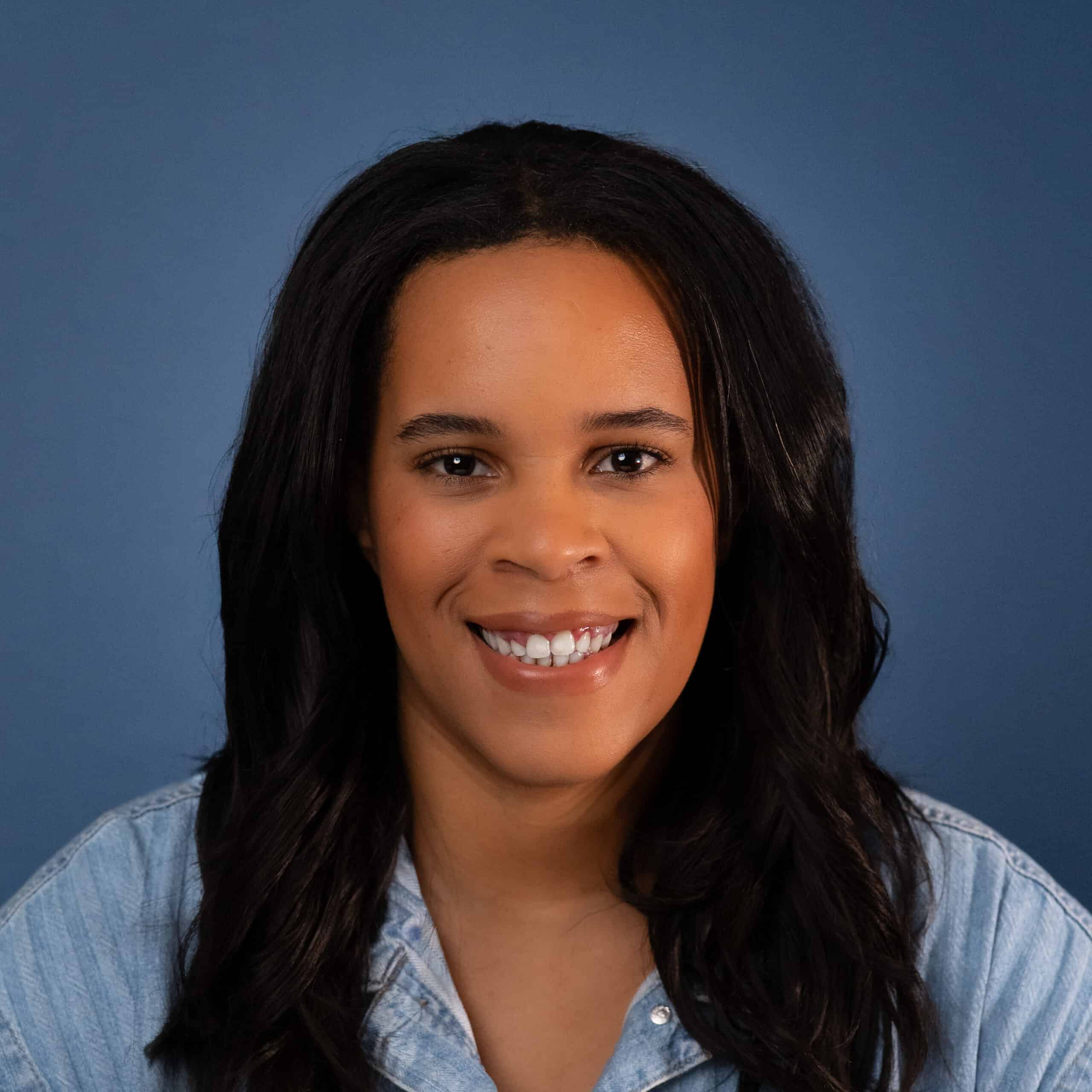 Akilah Boone smiles in a headshot, wearing a denim shirt against a blue background.