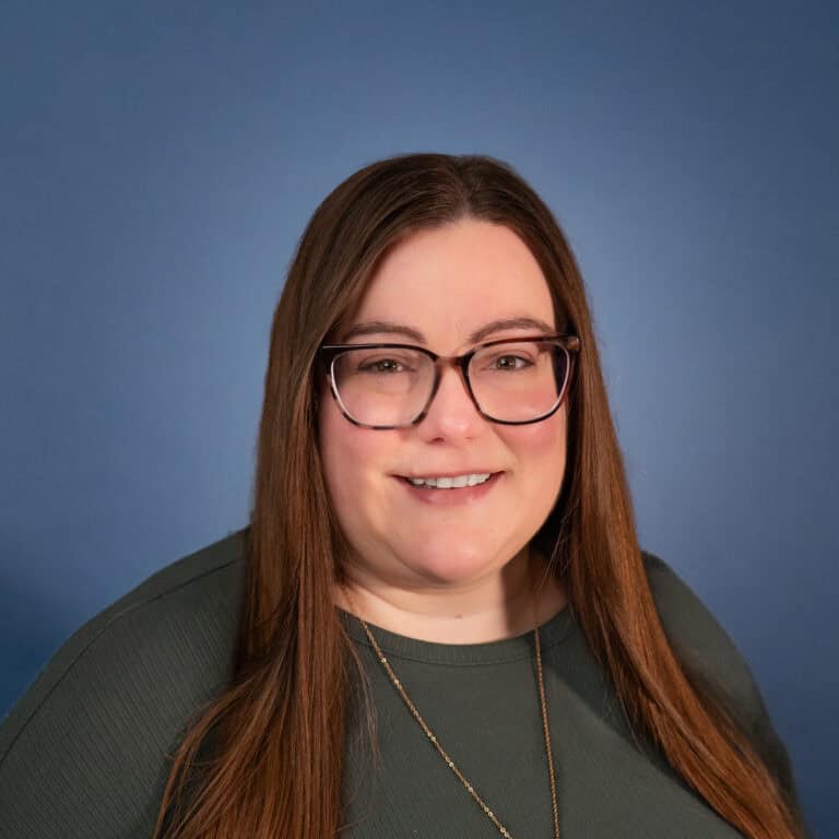 Allison Payton, smiling woman with glasses and long brown hair against a blue background.