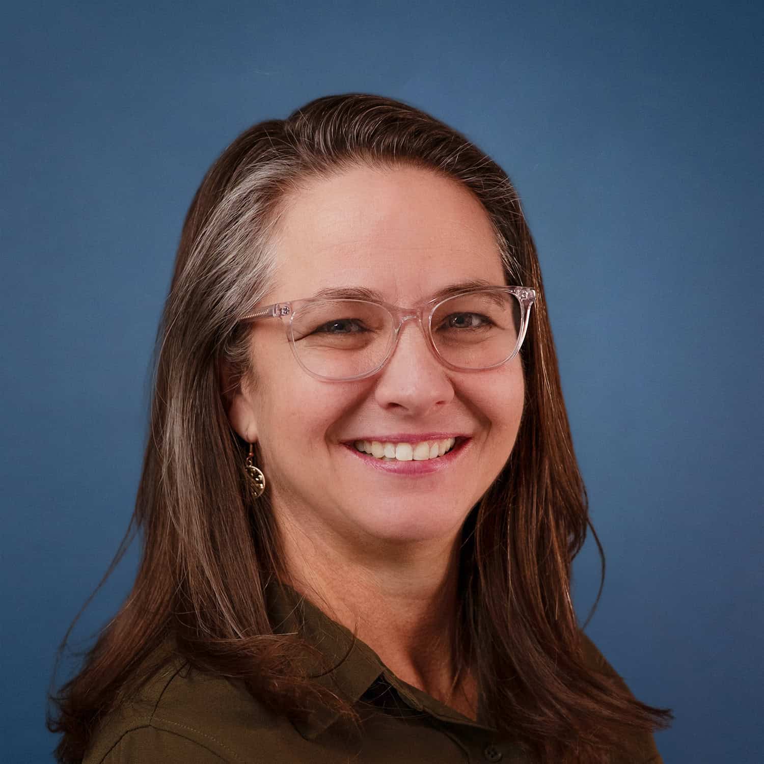 Portrait of Shanda Moon, smiling with glasses and long brown hair against a blue background.