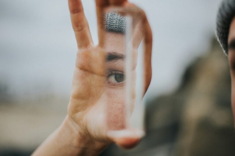 Eye and face partially visible through a distorted mirror held by a hand.