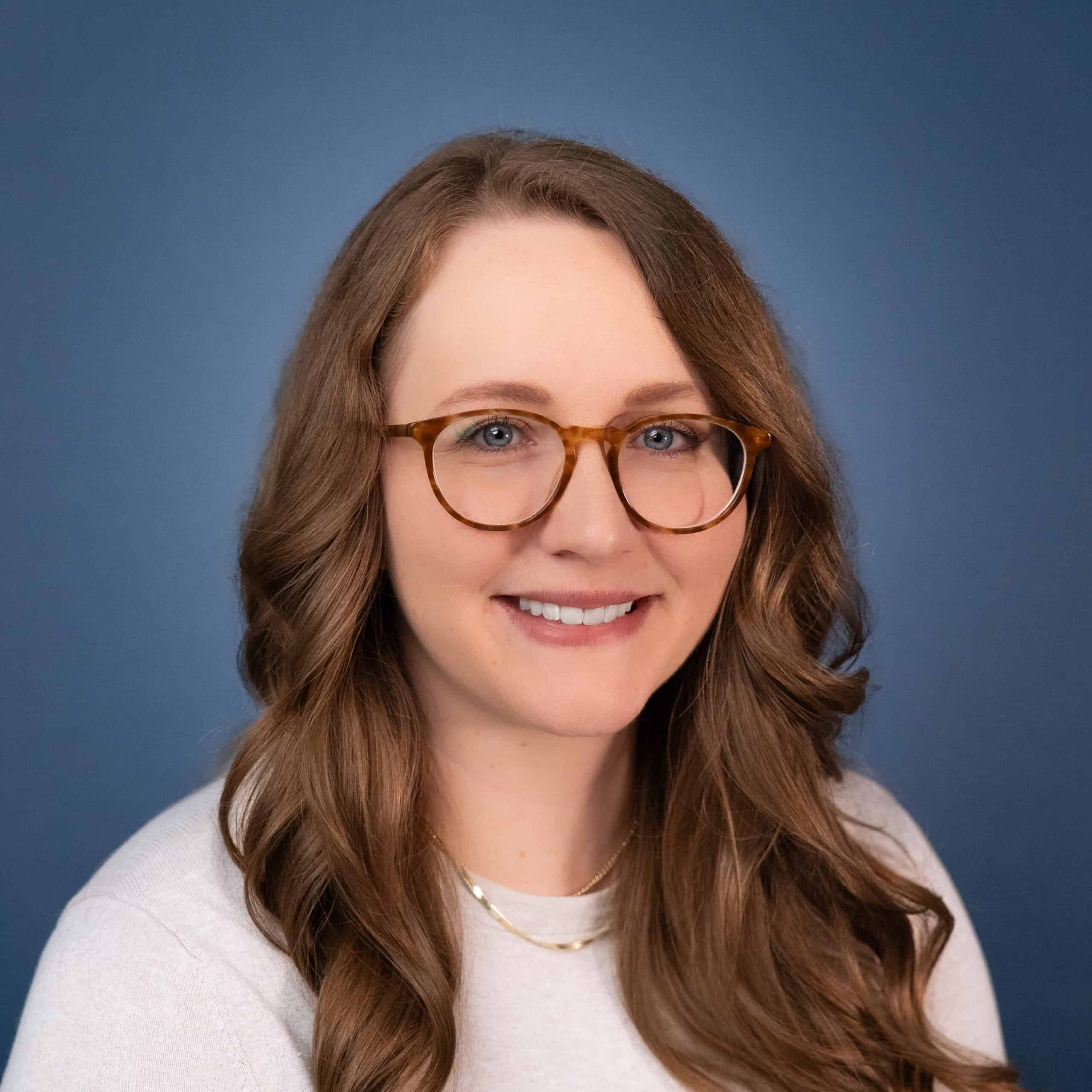 Ashtyn Fair headshot: Woman with long brown hair and glasses smiling