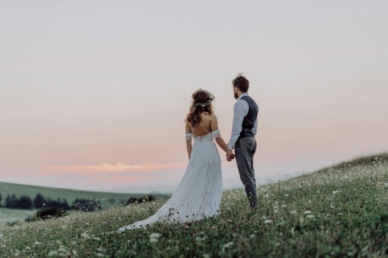 Bride and groom holding hands in a meadow at sunset.