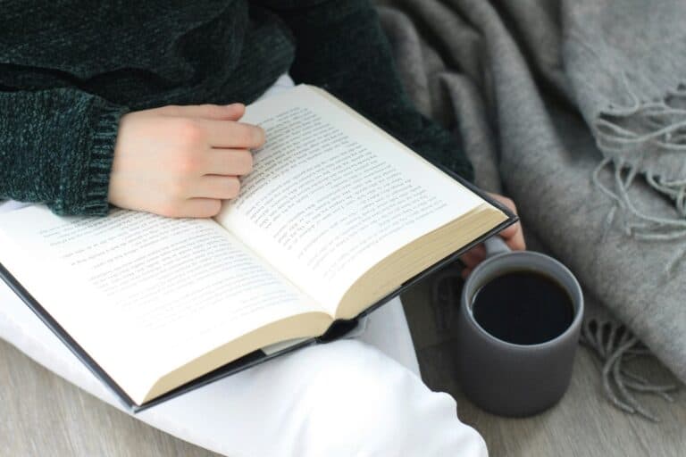 Person reading a book with coffee, cozy scene. Could relate to unfinished stories.