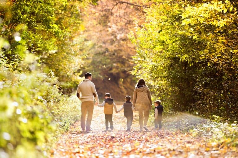 Family of five walking on a leaf-covered path in the autumn woods.