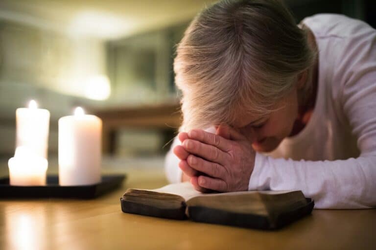 Woman praying over Bible by candlelight, expecting God's guidance.