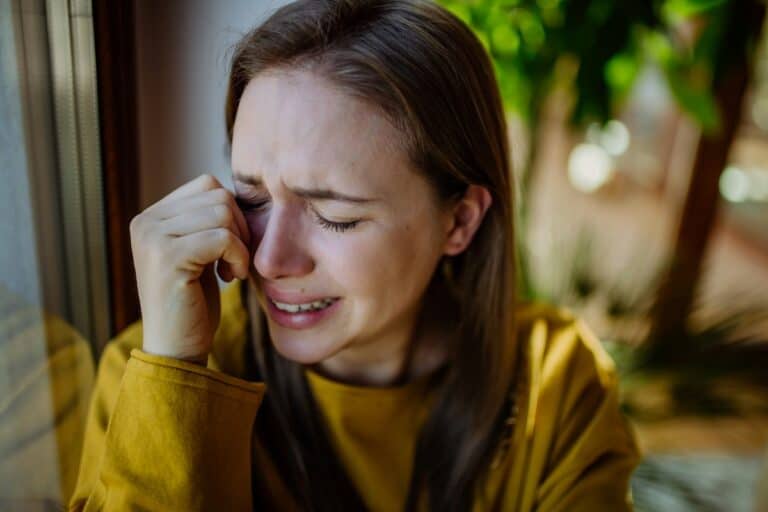Woman cries, wiping tears near window. Emotional distress, Ministry to My Soul theme.