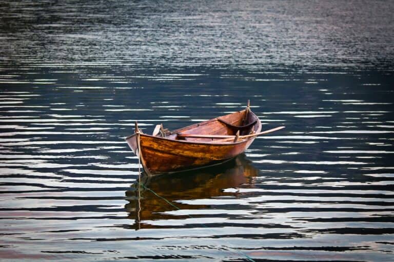 Wooden rowboat adrift on calm, rippled water. Reflective surface.