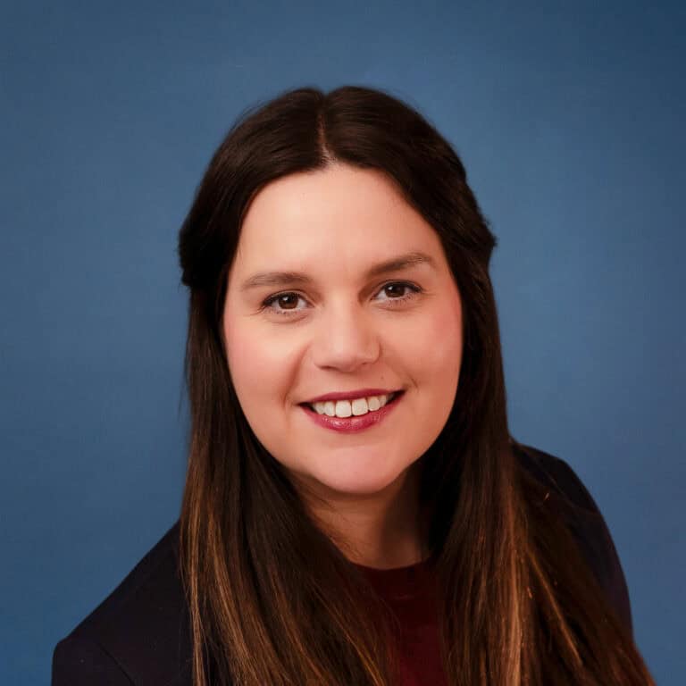 Daniela Close smiling in a professional headshot with a blue background.