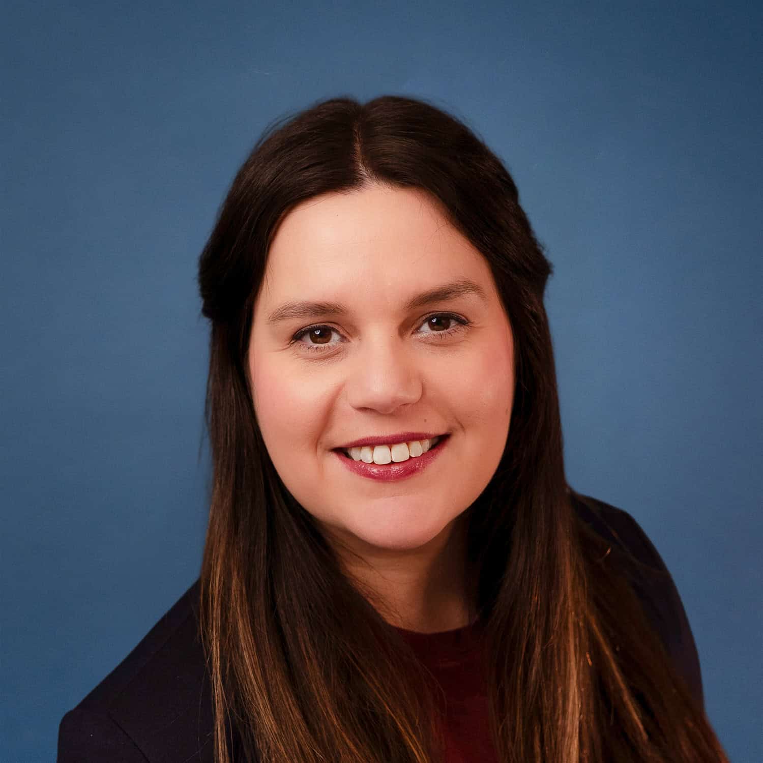 Daniela Close smiling in a professional headshot with a blue background.