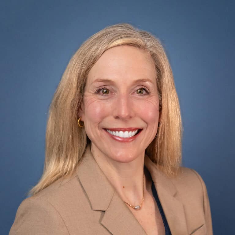 Professional headshot of Heather Peters smiling in a tan blazer against a blue background.