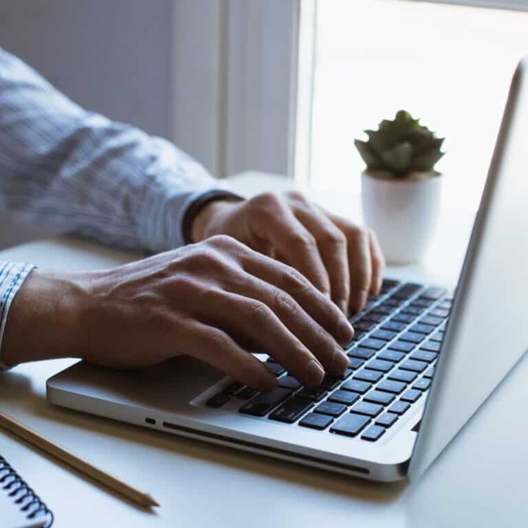 Hands typing on a laptop keyboard next to a small succulent and notebook.