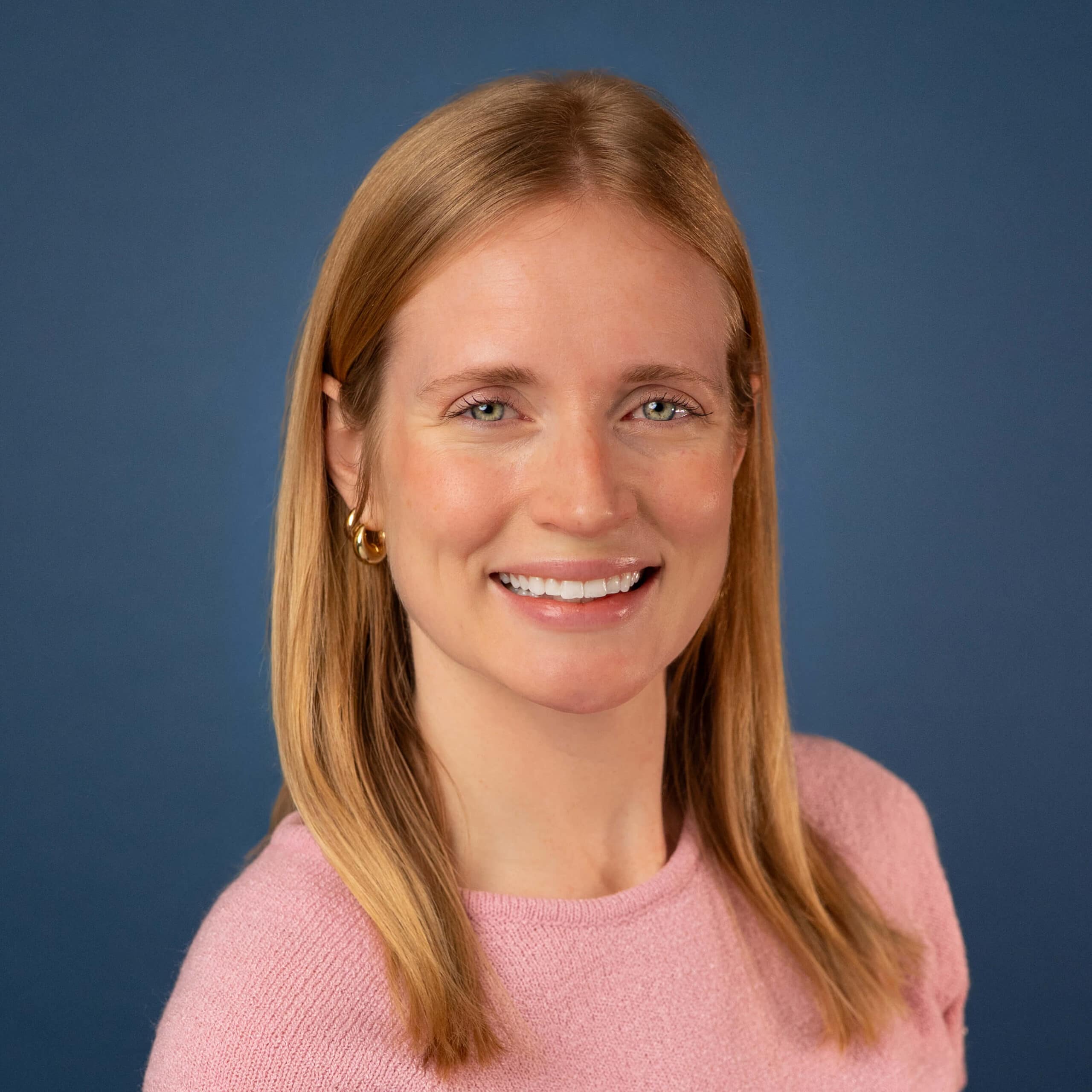 Abby Price headshot. Smiling woman with blonde hair and pink sweater against a blue background.