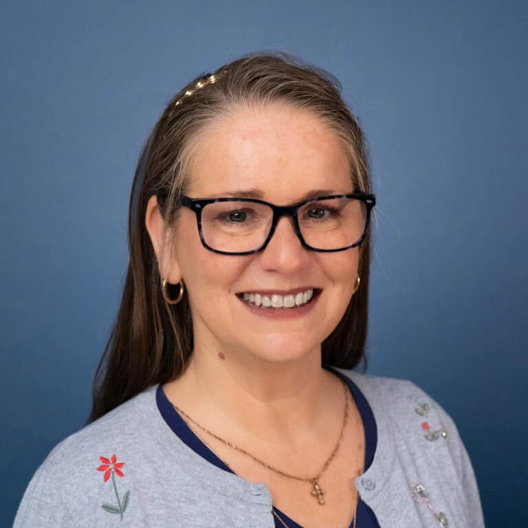 Smiling woman with glasses and embroidered cardigan. Christ Community Church.