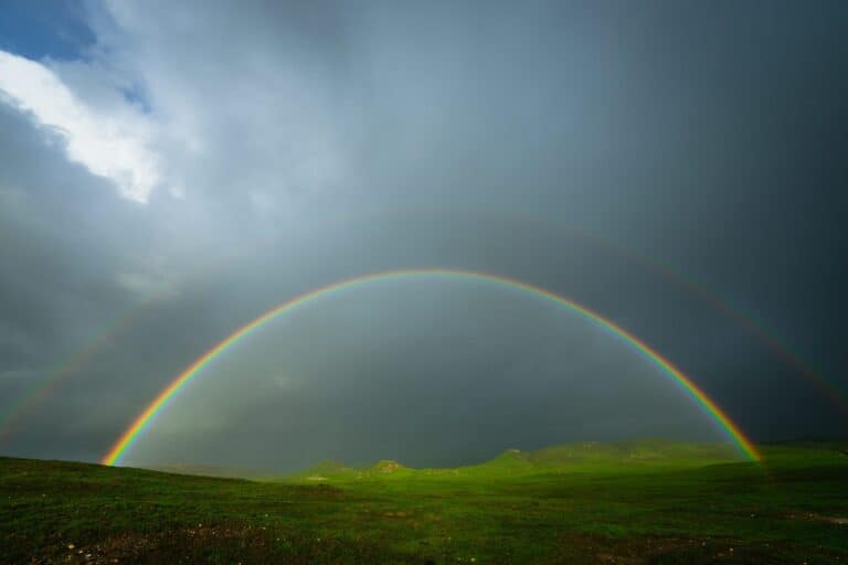 Double rainbow over a green field under a dramatic, stormy sky.