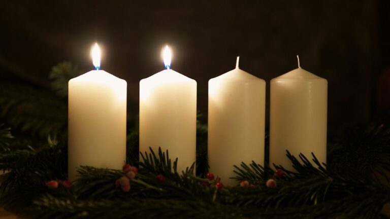 Advent wreath with two lit white candles surrounded by greenery and red berries.