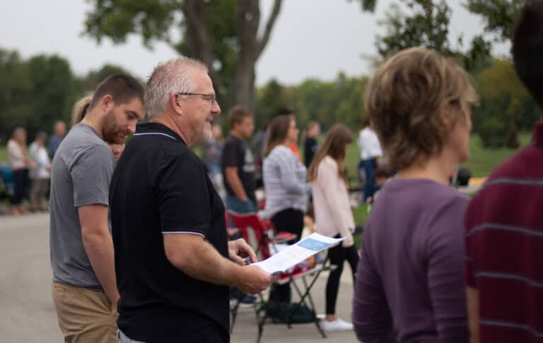Men's Ministries event: Men gathered outdoors, one holding a program at Christ Community Church.