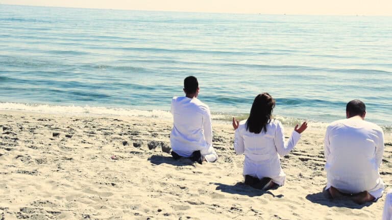 People in white robes kneel on beach, possibly for outreach.