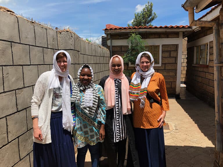 Four women in headscarves stand together, likely on outreach.
