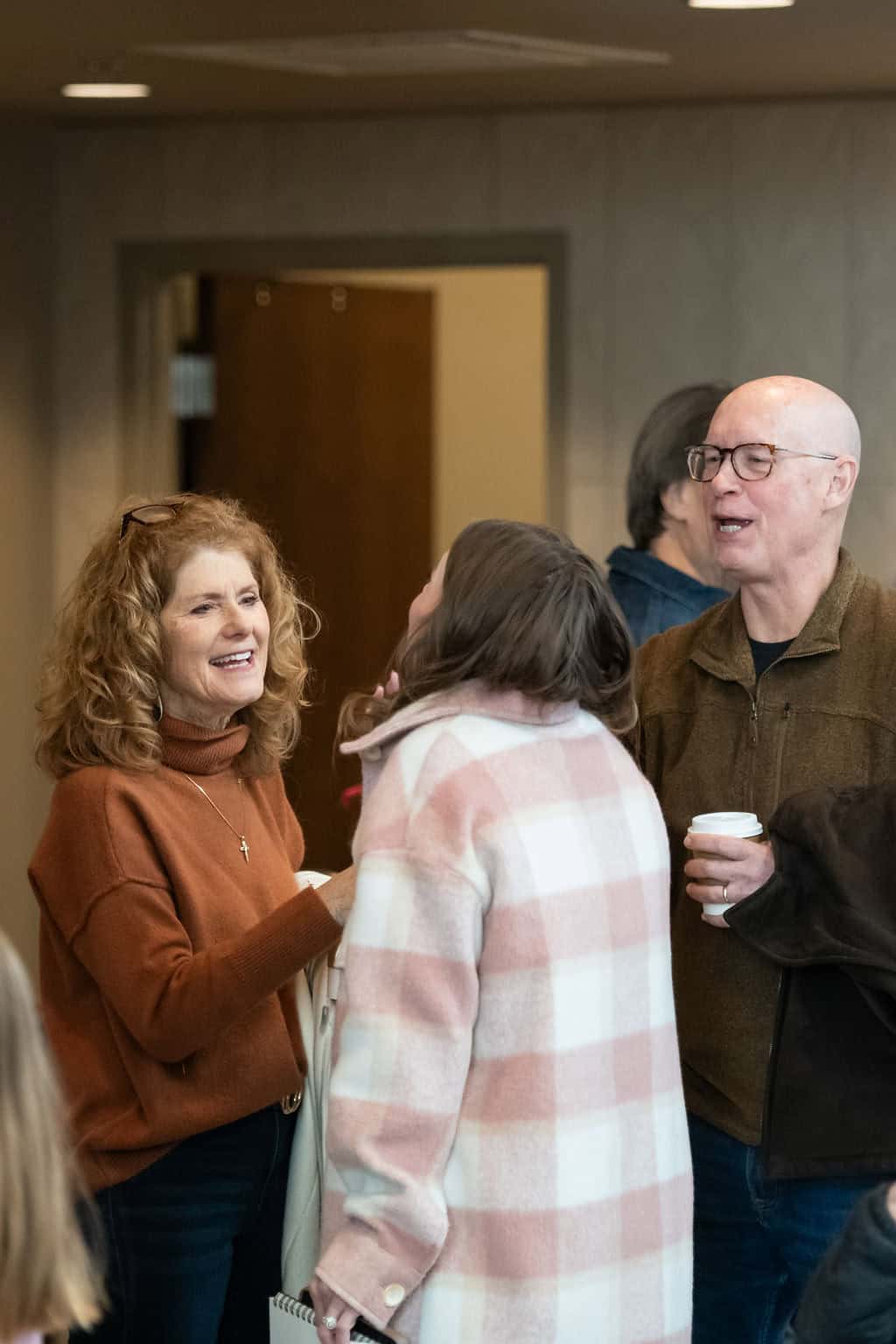 People talking at a Christ Community Church sermon event. Woman in orange sweater smiling.