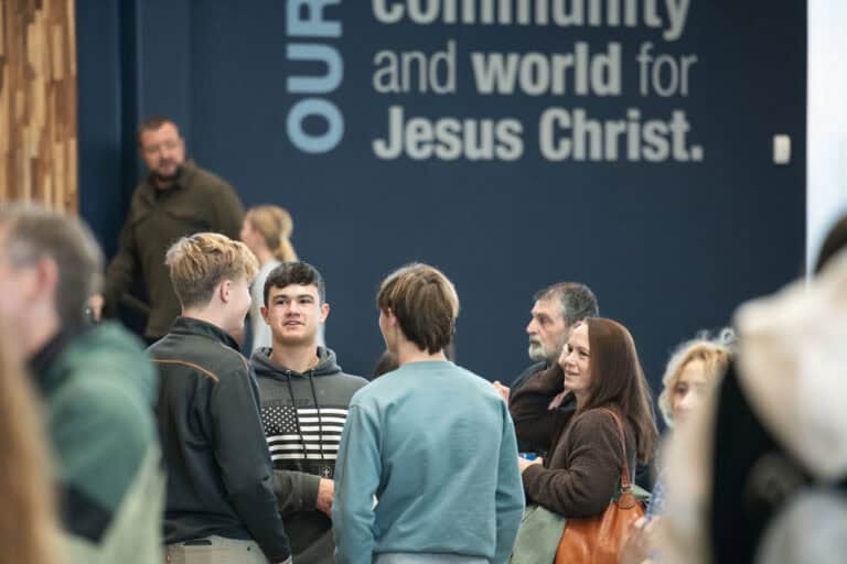 People gathering at Christ Community Church. "Our community and world for Jesus Christ" is visible on the wall.