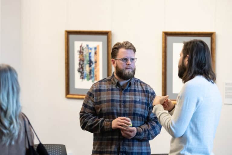 Two men discussing art at the Downtown Campus gallery, with framed artwork on the wall.