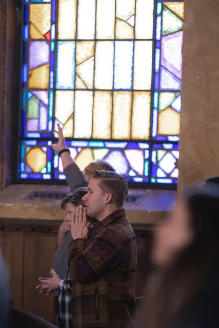 People praying during outreach at Christ Community Church. Stained glass window in background.