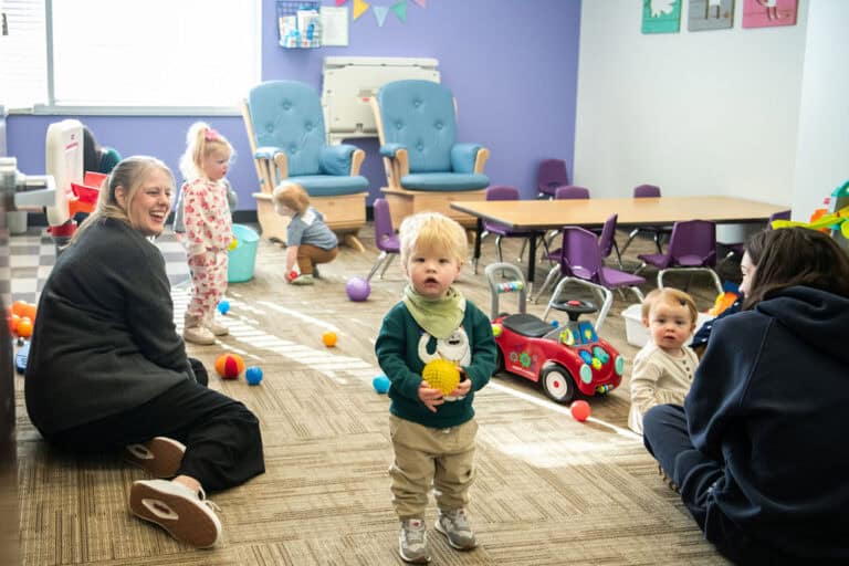 Children playing in a colorful daycare room, toys and caregivers present.