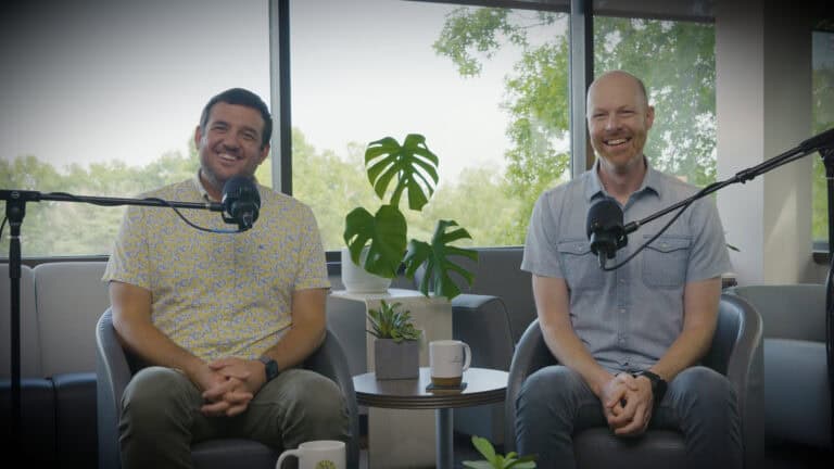 Two men smiling during a podcast recording in an office setting.