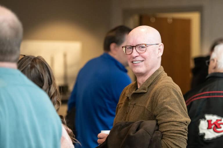 Man with glasses smiling at Olathe Campus event, wearing a brown jacket.