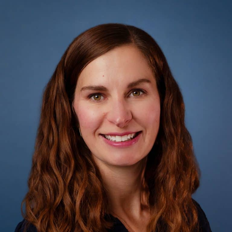 Headshot of Kelly Miller smiling against a blue background.
